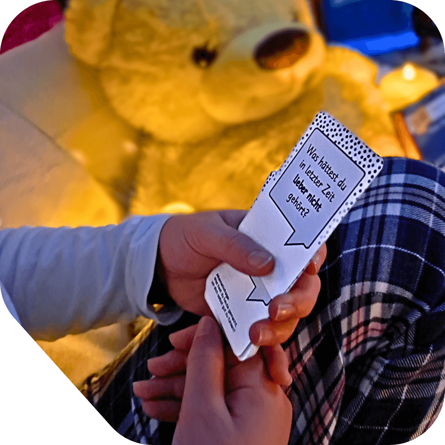 Kind hält einige Gesprächswunder-Karten von Set "Was war. Was wird. Meine Welt. Mein ich." in Händen. Im Hintergrund ist ein Plüschteddy zu sehen. Gemütliche Beleuchtung.