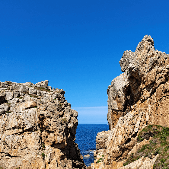 Ankündigungsbild Wundertiv Datenbank Blick zwischen zwei Felsen auf türkis Meer und blauen Himmel.