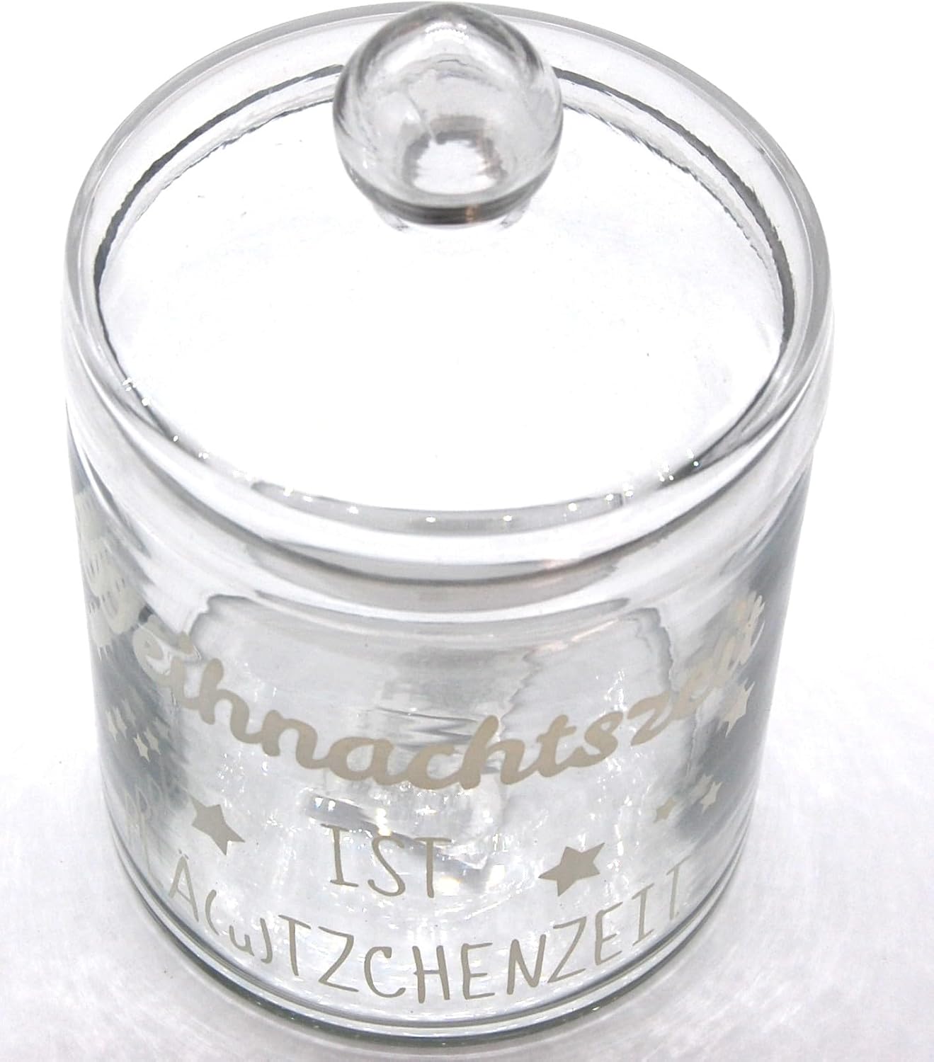 Hochwinkel-Aufnahme des Plätzchenglases aus Klarglas. Der witzige weiße Spruch "Weihnachtszeit ist Plä(u)tzchenzeit" ist deutlich sichtbar, umgeben von kleinen Sternen. Der Glasdeckel mit Griff ist aufgesetzt.